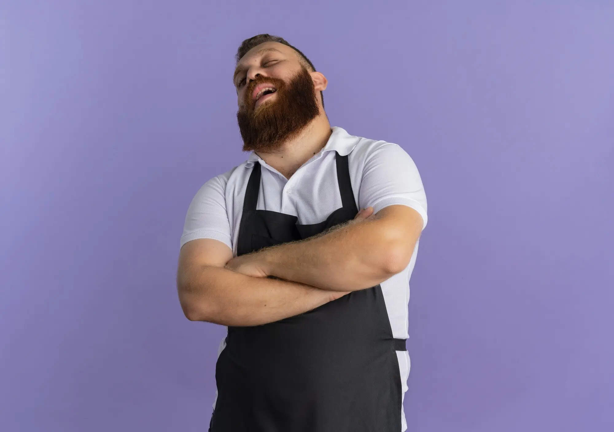 Genervter, professioneller, bärtiger, männlicher Barbier in Schürze mit vor der Brust verschränkten Armen steht vor einer violetten Wand, praxisnah und nachvollziehbar.